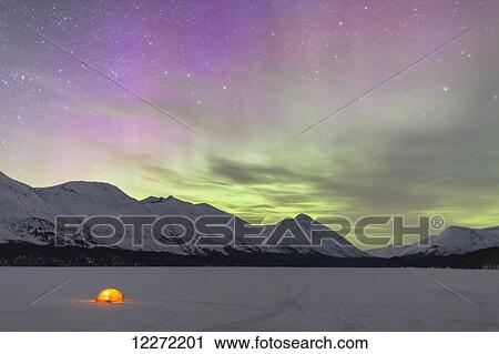 Stock Image - Nighttime view of a lit tent on a snow covered Trail Lake with the moon, stars, and Northern Lights overhead, Moose Pass, Kenai Peninsula, Southcentral Alaska. Fotosearch