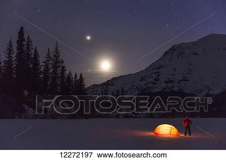 Nighttime view of a man standing next to a lit tent on a snow covered Trail Lake with the moon, stars, and planets overhead, Moose Pass, Kenai Peninsula, Southcentral Alaska View Large Photo Image Stock Photo - Nighttime view of a man standing next to a lit tent on a snow covered Trail Lake with the moon, stars, and planets overhead, Moose Pass, Kenai Peninsula, Southcentral Alaska. Fotosearch
