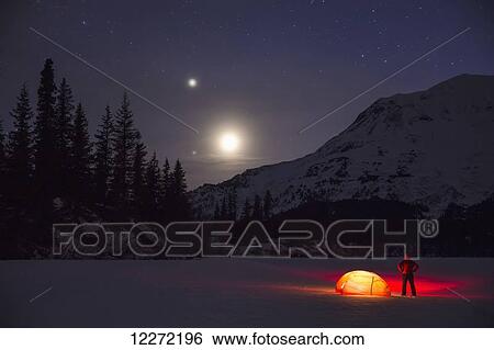Nighttime view of a man standing next to a lit tent on a snow covered Trail Lake with the moon, stars, and planets overhead, Moose Pass, Kenai Peninsula, Southcentral Alaska View Large Photo Image Stock Photograph - Nighttime view of a man standing next to a lit tent on a snow covered Trail Lake with the moon, stars, and planets overhead, Moose Pass, Kenai Peninsula, Southcentral Alaska. Fotosearch