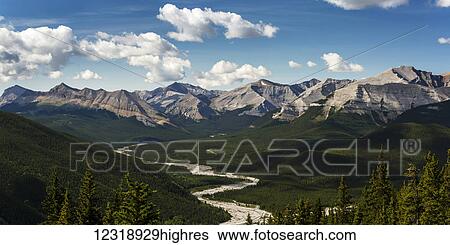 Stock Photograph - Panorama of river valley and mountain range with blue sky and clouds; Bragg Creek, Alberta, Canada. Fotosearch