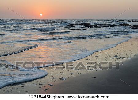 Peaceful and quiet sunset over the Atlantic ocean with orange and gold-coloured sun in the sky, sandy coastline and foam surf; Namibia View Large Photo Image Stock Photograph - Peaceful and quiet sunset over the Atlantic ocean with orange and gold-coloured sun in the sky, sandy coastline and foam surf; Namibia. Fotosearch