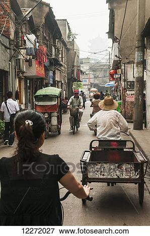 Stock Photo - Pedestrians and cyclists on an old street with a pagoda in the distance through the haze; Wuhan, Hubei province, China. Fotosearch