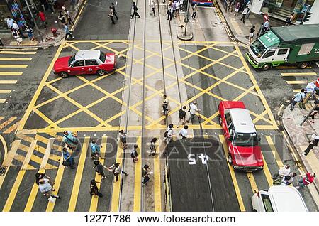 Stock Photograph - Pedestrians on a large crosswalk and traffic with taxis and trucks on a street; Hong Kong, China. Fotosearch