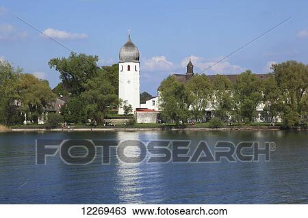 Stock Image - People along the water's edge of a lake and a tower with an onion shaped dome; Die Fraueninsel, Bayern, Germany. Fotosearch