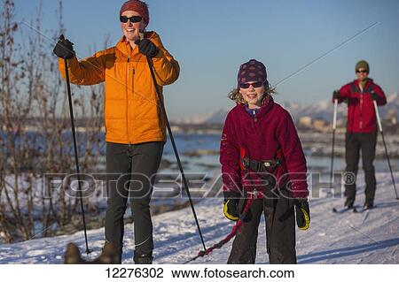 Stock Image - People cross country skiing on the Tony Knowles Coastal Trail near Earthquake Park with Anchorage skyline in the background, Cook Inlet, Southcentral Alaska. Fotosearch