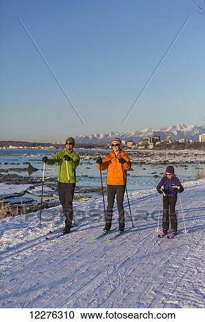 Stock Image - People cross country skiing on the Tony Knowles Coastal Trail near Earthquake Park with Anchorage skyline in the background, Cook Inlet, Southcentral Alaska. Fotosearch