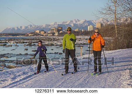 Stock Image - People cross country skiing on the Tony Knowles Coastal Trail near Earthquake Park with Anchorage skyline in the background, Cook Inlet, Southcentral Alaska. Fotosearch