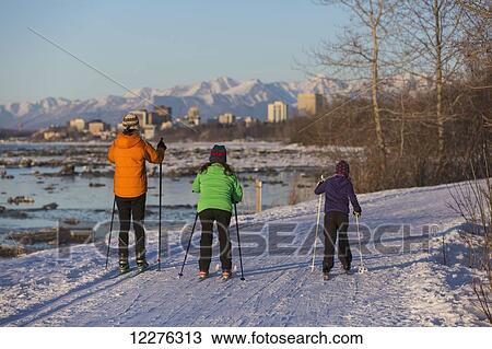 Stock Image - People cross country skiing on the Tony Knowles Coastal Trail near Earthquake Park with Anchorage skyline in the background, Cook Inlet, Southcentral Alaska. Fotosearch