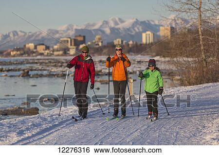 Stock Photograph - People cross country skiing on the Tony Knowles Coastal Trail near Earthquake Park with Anchorage skyline in the background, Cook Inlet, Southcentral Alaska. Fotosearch