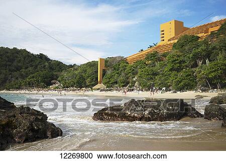 Stock Image - People on the beach and a large yellow hotel; Guerrero, Mexico. Fotosearch