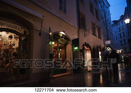 People stroll past shops in the pedestrianised streets of the old city on a rainy day; Salzburg, Austria View Large Photo Image Picture - People stroll past shops in the pedestrianised streets of the old city on a rainy day; Salzburg, Austria. Fotosearch