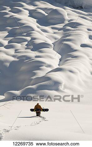 Stock Photography - Person walking with a snowboard in mountains above Haines, Southeast Alaska, USA. Fotosearch