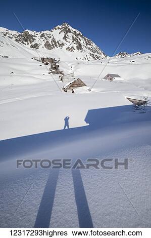 Stock Photograph - Photographer Doug Lindstrand takes a picture of his shadow in Hatcher Pass, near Independence Mine in late winter. The old delapidated mine buildings show in the snow in the background, near Palmer, South-central Alaska; Alaska, United States of America. Fotosearch