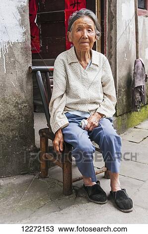 Stock Image - Portrait of a senior woman sitting in front of her house in a small village near Wuyuan; Jiangxi province, China. Fotosearch