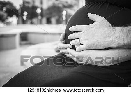 Stock Photograph - Pregnant couple holding hands on stomach; Waco, Texas, United States of America. Fotosearch