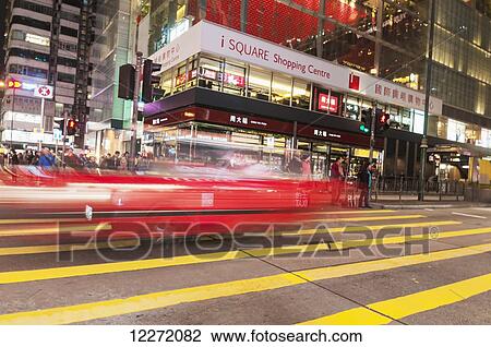Stock Image - Red taxi and pedestrians along Nathan Road in front of Chungking Mansions; Hong Kong, China. Fotosearch