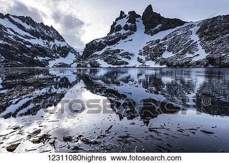 Stock Photograph - Reflections of snow covered rugged mountains in water; Antarctica. Fotosearch
