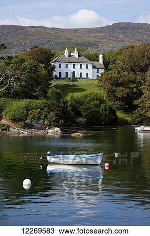 Rowboats moored in the tranquil water with a large white house on the shore, near Castlecove; County Kerry, Ireland View Large Photo Image Stock Image - Rowboats moored in the tranquil water with a large white house on the shore, near Castlecove; County Kerry, Ireland. Fotosearch