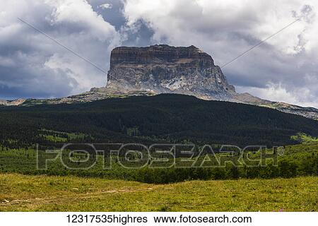 Stock Photograph - Rugged rock formation under cloudy sky with lush green vegetation; Montana, United States of America. Fotosearch