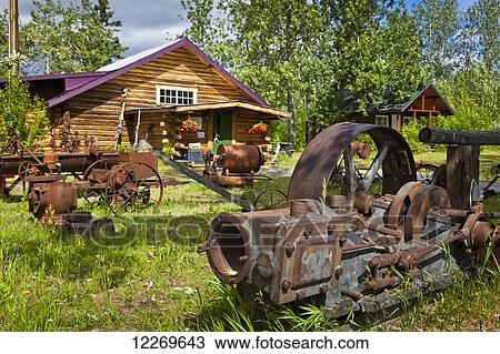 Stock Image - Rustic building at Carriage House Restaurant and old mining equipment at Historic Gakona Lodge & Trading Post, Gakona, Southcentral Alaska, Summer.. Fotosearch