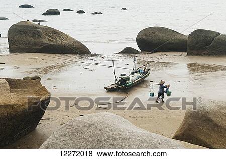 Scene of a fisherman carrying his supplies near to his boat around some rocks on Xiamen's beach; Xiamen, Fujian Province, China View Large Photo Image Stock Photo - Scene of a fisherman carrying his supplies near to his boat around some rocks on Xiamen's beach; Xiamen, Fujian Province, China. Fotosearch