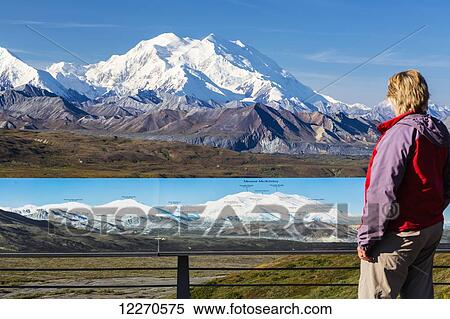 Stock Photography - Scenic view of Mt. McKinley from Eielson Visitor Center with a woman visitor and tourist information board in the foreground in Denali National Park, Interior Alaska, Summer, USA.. Fotosearch
