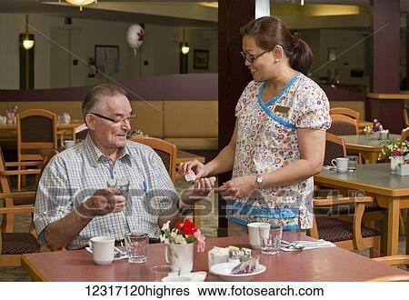 Stock Photograph - Senior Citizen Receiving Medication from Caregiver; Devon, Alberta, Canada. Fotosearch