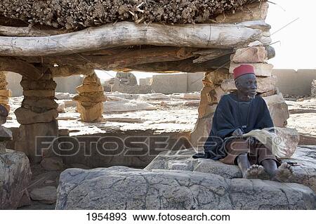 Stock Image - Senior man in front of the Toguna (House of Words) in Sangha, Mali. Fotosearch