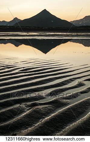 Silhouette of a peaked mountain reflected in tranquil water and ripples in the sand at sunset; Alaska, United States of America View Large Photo Image Stock Photograph - Silhouette of a peaked mountain reflected in tranquil water and ripples in the sand at sunset; Alaska, United States of America. Fotosearch