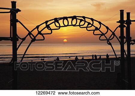 Stock Image - Silhouette of a playground structure on the beach and a golden sunset over the ocean; Ciclana de la Frontera, Andalusia, Spain. Fotosearch