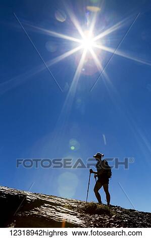 Stock Photograph - Silhouette of female hiker on rocky ridge with blue sky and sunburst; Waterton, Alberta, Canada. Fotosearch