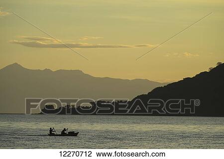 Stock Image - Silhouette of fishermen in dugout canoe leaving Cape Maclear in the evening, Lake Malawi; Malawi. Fotosearch