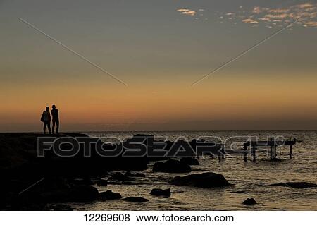 Stock Photo - Silhouette of two people standing at the water's edge watching the sunset over the water; Paphos, Cyprus. Fotosearch
