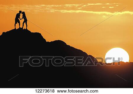 Stock Photo - Silhouetted couple kissing on a big rock at sunset; Oahu, Hawaii, United States of America. Fotosearch