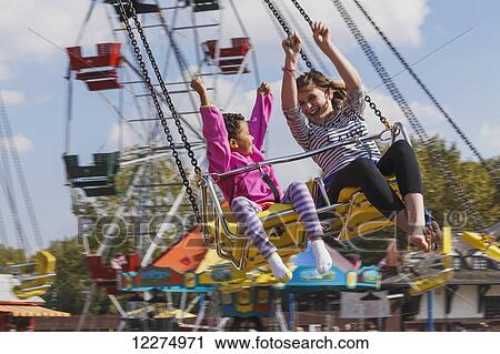 Stock Image - Sisters (aged 5 and 12) enjoying a swing ride; Edmonton, Alberta, Canada. Fotosearch