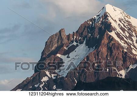 Stock Photograph - Snow-capped rugged mountain peak with blue sky and cloud. Fotosearch