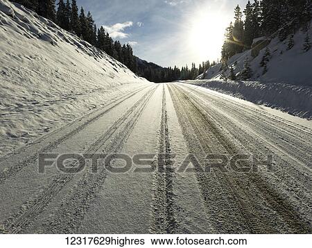 Stock Photograph - Snow covered road with tire tracks in Jasper National Park; Alberta, Canada. Fotosearch