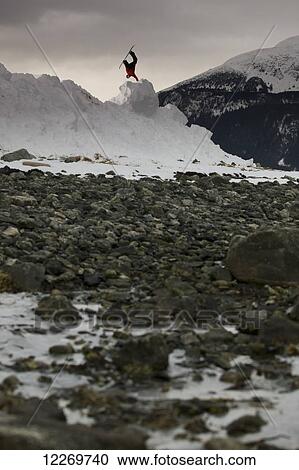 Stock Image - Snowboarder makes a jump on a snow hill with rocks in the foreground, Haines, Southeast Alaska. Fotosearch