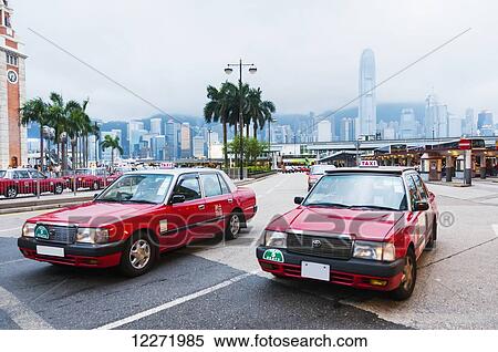 Stock Photography - Some red taxis in Kowloon with the skyline of Hong Kong Island as background; Kowloon, Hong Kong, China. Fotosearch