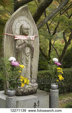 Stock Photo - Statue of a standing Buddha and flowers; Kyoto, Japan. Fotosearch