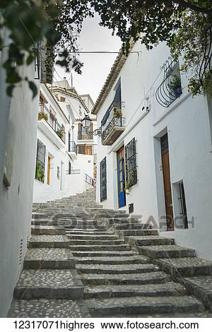 Stock Photograph - Steps up a sloped street in the beautiful town of Altea in Costa Blanca, where the houses are painted with the typical Mediterranean colours, white walls and blue doors and windows; Altea, Alicante, Spain. Fotosearch