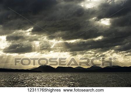 Stock Photograph - Sun rays through the dark clouds at sunset over Douglas Channel; British Columbia, Canada. Fotosearch