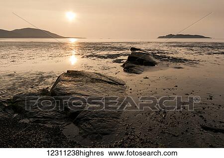 Stock Photograph - Sunlight glowing at sunset and reflected on the wet beach and ocean. Fotosearch