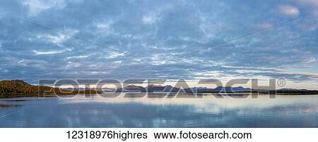 Stock Photograph - Sunrise on the calm waters of Tikchik Lake, patchy clouds in the background, Wood Tikchik State Park, Southwestern Alaska; Alaska, United States of America. Fotosearch