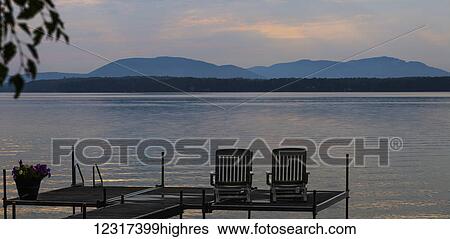 Stock Photograph - Sunset on lake with silhouetted chairs on wharf; Knowlton, Quebec, Canada. Fotosearch