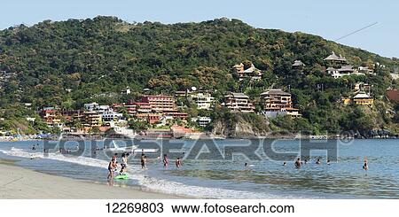Stock Image - Swimming in the water off the beach and houses on the hillside along the coast; Guerrero, Mexico. Fotosearch