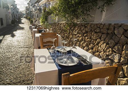Stock Photograph - Tables for dining along a street in the beautiful town of Altea in Costa Blanca; Altea, Alicante, Spain. Fotosearch