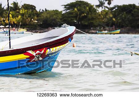 Stock Image - The front of a colourful painted boat tied in bay with beach and trees in the background; Akumal, Quintana Roo, Mexico. Fotosearch