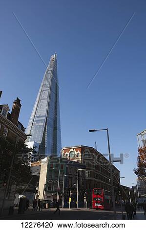 Stock Image - The Shard skyscraper by Renzo Piano rising above historic buildings on Tooley Street, with a red London double-decker bus in foreground; London, England. Fotosearch