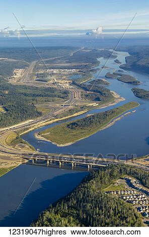 Stock Photograph - This aerial view shows the city of Fort McMurray Alberta and the Athabasca River with the oil sands regional production mines viewed in the far distance of the river; Fort McMurray, Alberta, Canada. Fotosearch